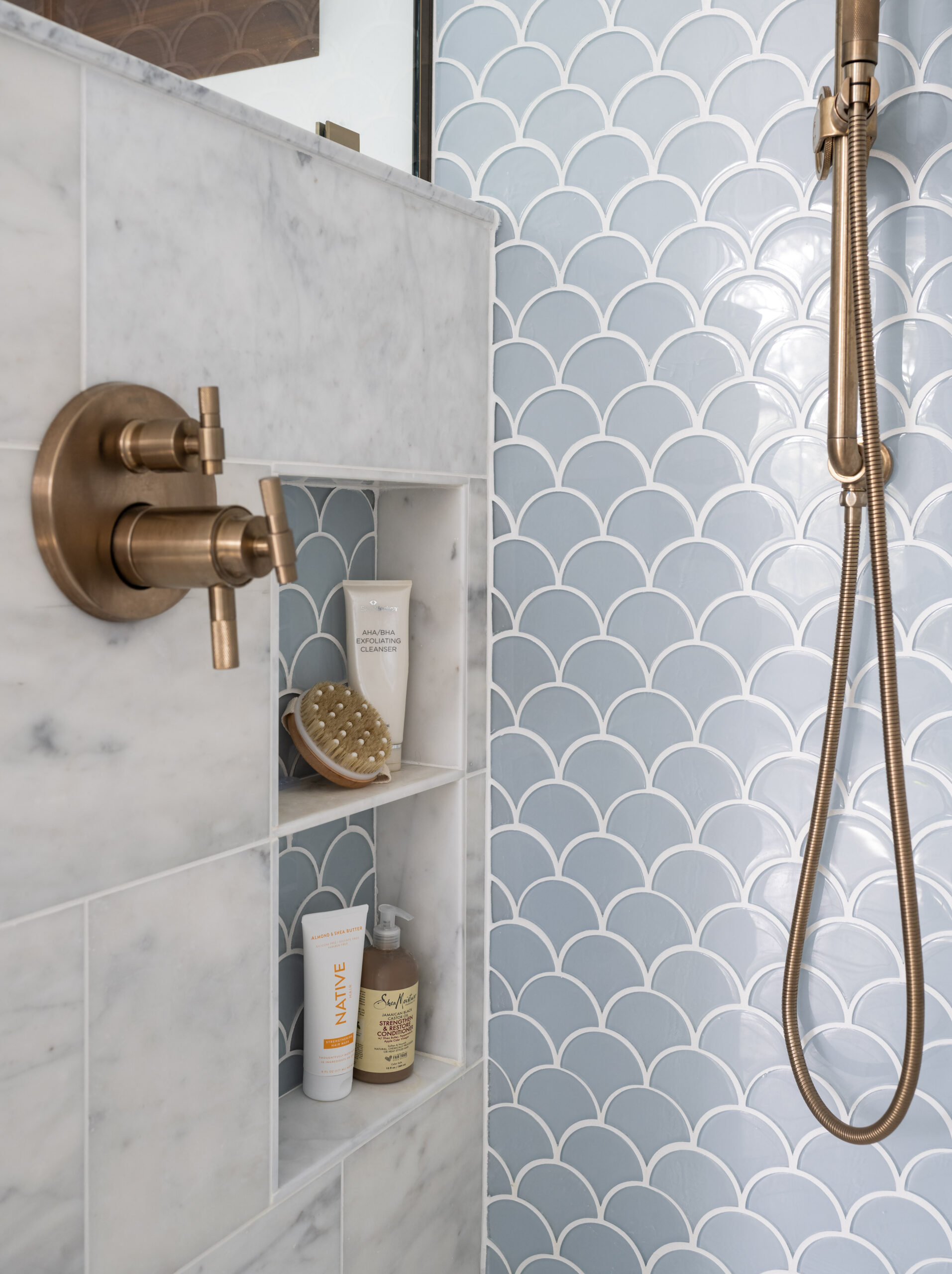 Luxury shower with hidden niche and luxe gold finishes and light blue scallop tile design by JP Hoffman Design Build